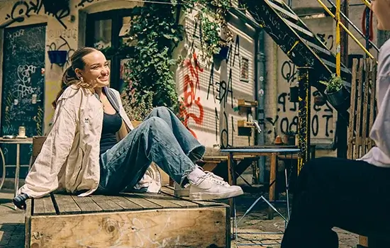 En efterskoleelev sidder og slapper af i et urbant miljø med street art i baggrunden.