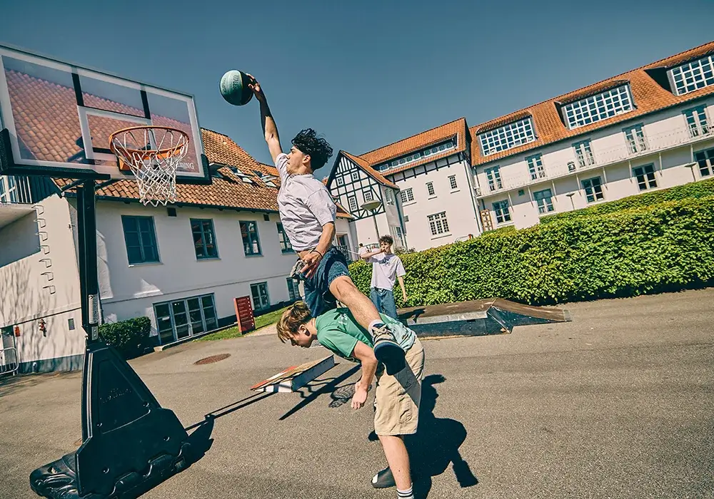 To drenge spiller basketball og laver et dunk på skolens udendørsbane i Risskov.