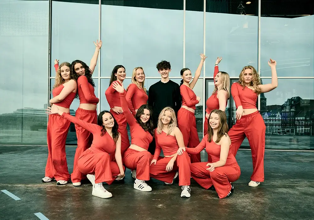 Holdfoto af glade efterskoleelever i rødt dansetøj, der poserer sammen på en tagterrasse i Aarhus.