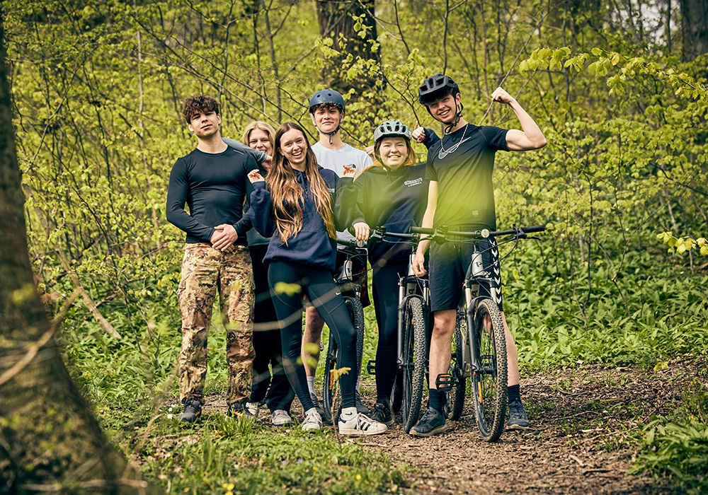 Et smilende hold af adventure-elever poserer med deres mountainbikes i den grønne natur ved Aarhus.