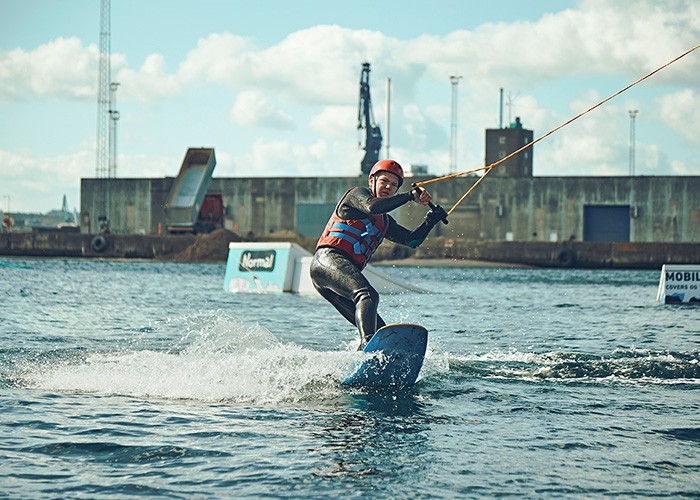 En efterskoleelev står på wakeboard i Aarhus Bugt og mestrer vandsportens teknikker.