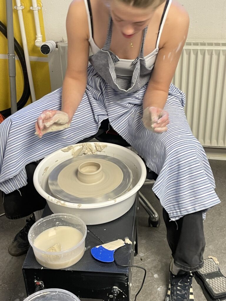 En elev på efterskole keramik-holdet arbejder koncentreret med at forme ler på en drejeskive.
